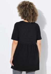 Černá tuniková košile s krátkým rukávem vyrobená z měkké tkaniny, s nařaseným pasem a volnou siluetou. Jednoduchý design bez vzorů.