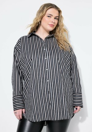 Camicia oversize a righe bianche e nere con colletto a punta, chiusura con bottoni e maniche lunghe. La texture appare liscia con una vestibilità comoda.