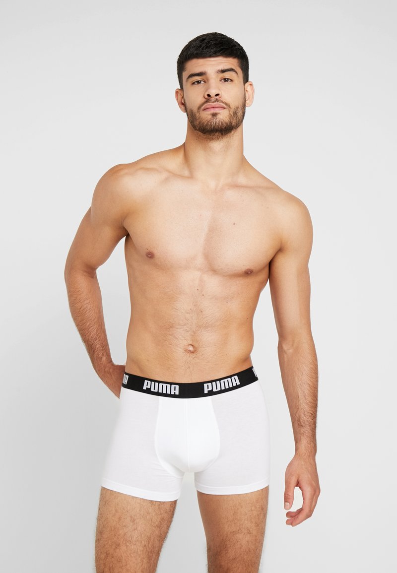 Valged poksipüksid musta elastse vöökohtaga, millel on "PUMA" logo. Sile materjal, stiilne lõige, keskpõlve pikkus ja tavaline lõige.