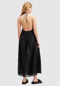 Abito maxi nero con scollo all'americana, schiena bassa e vita elastica. Realizzato in materiale leggero e trasparente. Indossato con scarpe piatte nere senza lacci.