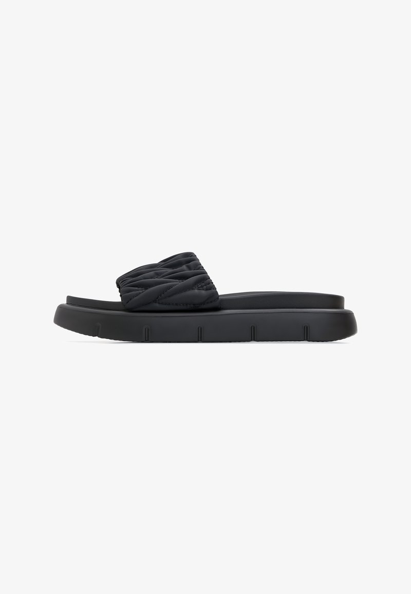 Sandales à enfiler noires avec dessus matelassé, semelle en caoutchouc plate avec rainures, et design minimaliste. Texture douce sur toute la surface.