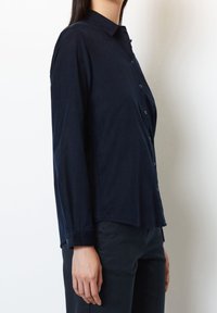 Ciemnogranatowa koszula na długi rękaw, zapinana na guziki, z kołnierzykiem, prostym krojem, guzikami z przodu oraz gładką fakturą tkaniny. Dół koszuli jest lekko zaokrąglony.