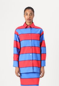 Napapaita, jossa on vaakasuoria punaisia ja sinisiä raitoja, kaksi rintataskua sekä kauluksellinen kaula-aukko metallisten napitusnappien kanssa.