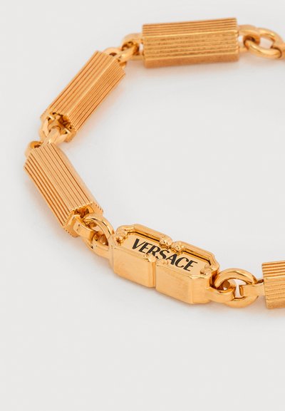 Χρυσό βραχιόλι με υφή ορθογώνιων συνδέσμων και κούμπωμα χαραγμένο με το όνομα της μάρκας "Versace" με μαύρα γράμματα.