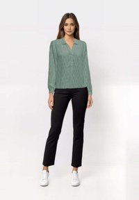 Blusa a maniche lunghe verde con motivo e colletto, abbinata a pantaloni neri e sneakers bianche, caratterizzata da una vestibilità slim e una texture liscia.