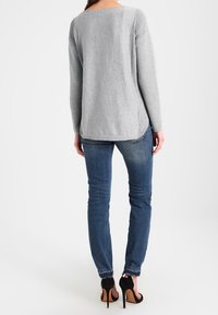 Grauer Strickoberteil mit gerippten Seitendetails, kombiniert mit blauen Skinny Jeans und schwarzen High Heels, von hinten betrachtet.