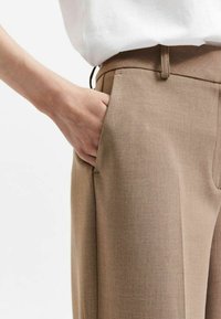 Bruine op maat gemaakte broek met een gladde textuur, voorzien van een zijzak en een rechte pijp. Gecombineerd met een witte top.