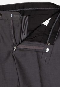 Grau zugeschnittene Hosen, aufgeklappt, mit einem Reißverschluss, zwei Knöpfen und einem glatten Innenfutter, auf dem ein Pflegeetikett sichtbar ist.