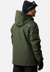 Grön isolerad jacka med huva, som har en slät yta, justerbara manschetter och varumärkesnamnet på baksidan nära nacken.