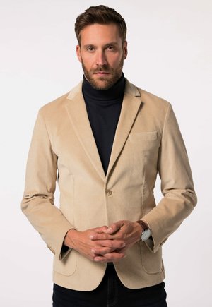 Beige Cordblazer mit Reverskragen, einer Knopfschließe und einer Brusttasche. Über einem schwarzen Rollkragenpullover getragen.