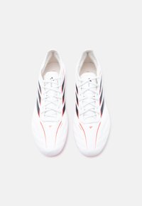 Ζευγάρι λευκών ποδοσφαιρικών παπουτσιών με μαύρες ρίγες και κόκκινες λεπτομέρειες, απεικονιζόμενα από πάνω σε απλό λευκό φόντο.