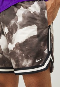 Nike lühikesed püksid, kus on pruun ja valge abstraktne muster, võrgufabric ja mustad ja valged triibud ääres. Logo alumisel jalal.