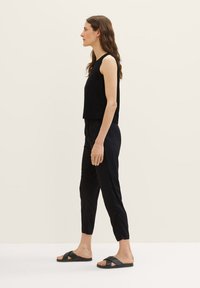 Zwarte mouwloze top gecombineerd met zwarte tapered broek, beide in een gladde stof. Zwarte sandalen met brede banden. Eenvoudig, minimalistisch design.