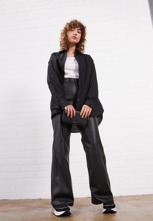 Black oversized button-up shirt over a white tank top, paired with high-waisted, shiny black faux leather pants and black and white sneakers.