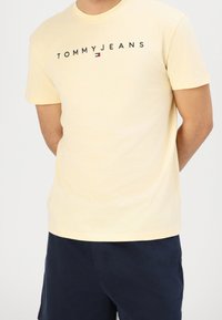 Żółta bawełniana koszulka z krótkim rękawem z napisem "TOMMYJEANS" w czarnych literach oraz małym akcentem logo. Klasyczny krój.