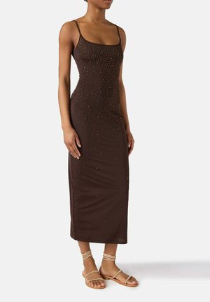 Donna che indossa un vestito midi senza maniche marrone scuro con piccole decorazioni di perline e sandali piatti beige con cinturini.