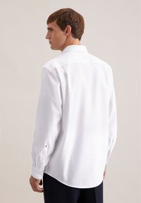 Biała koszula z długim rękawem, klasycznym kołnierzem, gładką fakturą i mankietami zapinanymi na guziki, z zakrzywionym dołem i subtelnym logo.