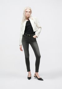 Λευκή cropped δερμάτινη ζακέτα πάνω από μαύρο πουκάμισο, συνδυασμένη με γκρίζα skinny τζιν και μαύρες γόβες. Απλή λεπτομέρεια από μαύρο choker.