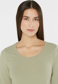Long-sleeved top in light green, featuring a rounded neckline and smooth, lightweight fabric. Simple design with no notable patterns or accents.