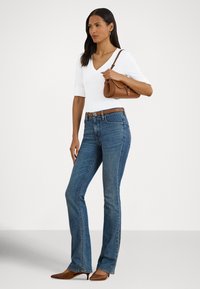 Zili izplestie džinsi ar vidēju vidukli, kopā ar pieguļošu baltu V veida kakla kreklu. Brūna josta ar logotipa detaļām un maza brūna rokassoma.