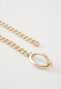 Bracelet en chaîne dorée avec des maillons entrelacés et un grand fermoir ovale. Texture lisse avec une finition polie et un détail de logo gravé.