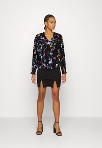 Blusa preta com flores, de mangas longas e decote em v, combinada com uma saia mini preta de cintura alta, com uma abertura frontal. Sandálias de salto pretas.