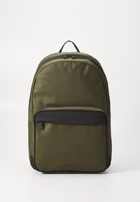 Olivengrønn ryggsekk laget av glatt nylon, med et hovedrom med glidelås og en svart frontlomme med glidelås, samt et håndtak på toppen.