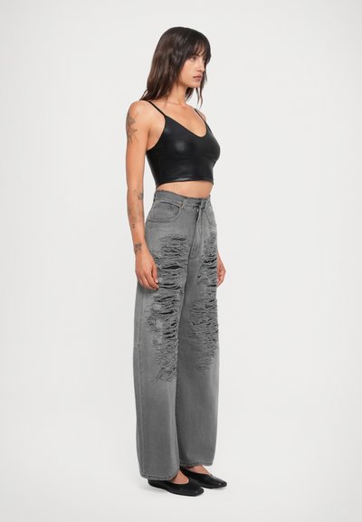 Plati pelēki džinsi ar nolietojumu un saplēstiem malām, apvienoti ar piegulošu melnu crop top un melnām zābakām.
