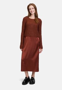 Maglione corto lavorato a maglia marrone con maniche lunghe abbinato a una gonna maxi in raso color ruggine e scarpe chunky nere.