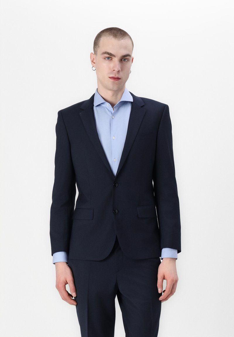 Marineblauw pak met slim fit ontwerp, voorzien van een enkelgeknoopte jas, notch revers en lichtblauwe accenten op het shirt.