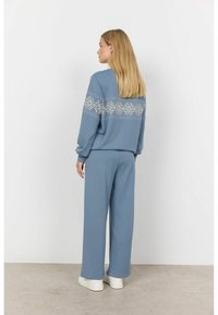 Lichtblauwe loungewear-set van zachte stof. De top heeft een wit sneeuwvlokkenpatroon op de achterkant. Loszittende broeken maken de look compleet.