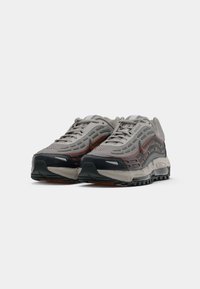 Pelēku un melnu Nike Air Max sporta apavu pāris ar sarkaniem akcentiem, sasietām auklām, novietoti viens otram blakus uz balta fona.