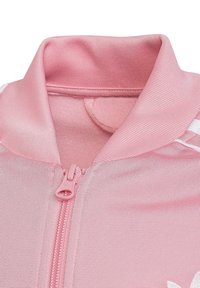 Rosa Sportjacke mit Stehkragen, Frontreißverschluss und glattem Stoff mit subtiler Glanzoptik. Weißes Akzentlogo auf der Brust.