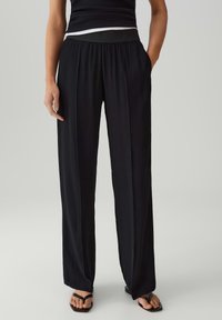 Pantaloni neri a gamba larga con vita alta elastica e tasche laterali; realizzati in un tessuto morbido e leggero con una texture liscia.