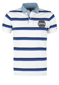 Polo à manches courtes en blanc avec des rayures horizontales bleues et navy. Il dispose d'un col en denim et d'un écusson rond sur la poitrine.