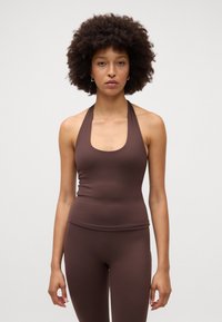 Ruda halterio kaklo tank top'as iš lygaus, elastingo audinio, prigludęs prie kūno per liemenį su apvaliu iškirpimu, derinamas su tinkamais prigludusiais leggingais.