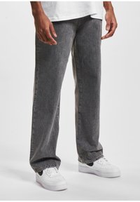 Pantalones de mezclilla gris con un corte holgado, que presentan una ligera textura y un acabado desgastado. Llevados con zapatillas blancas, que destacan un acento negro.