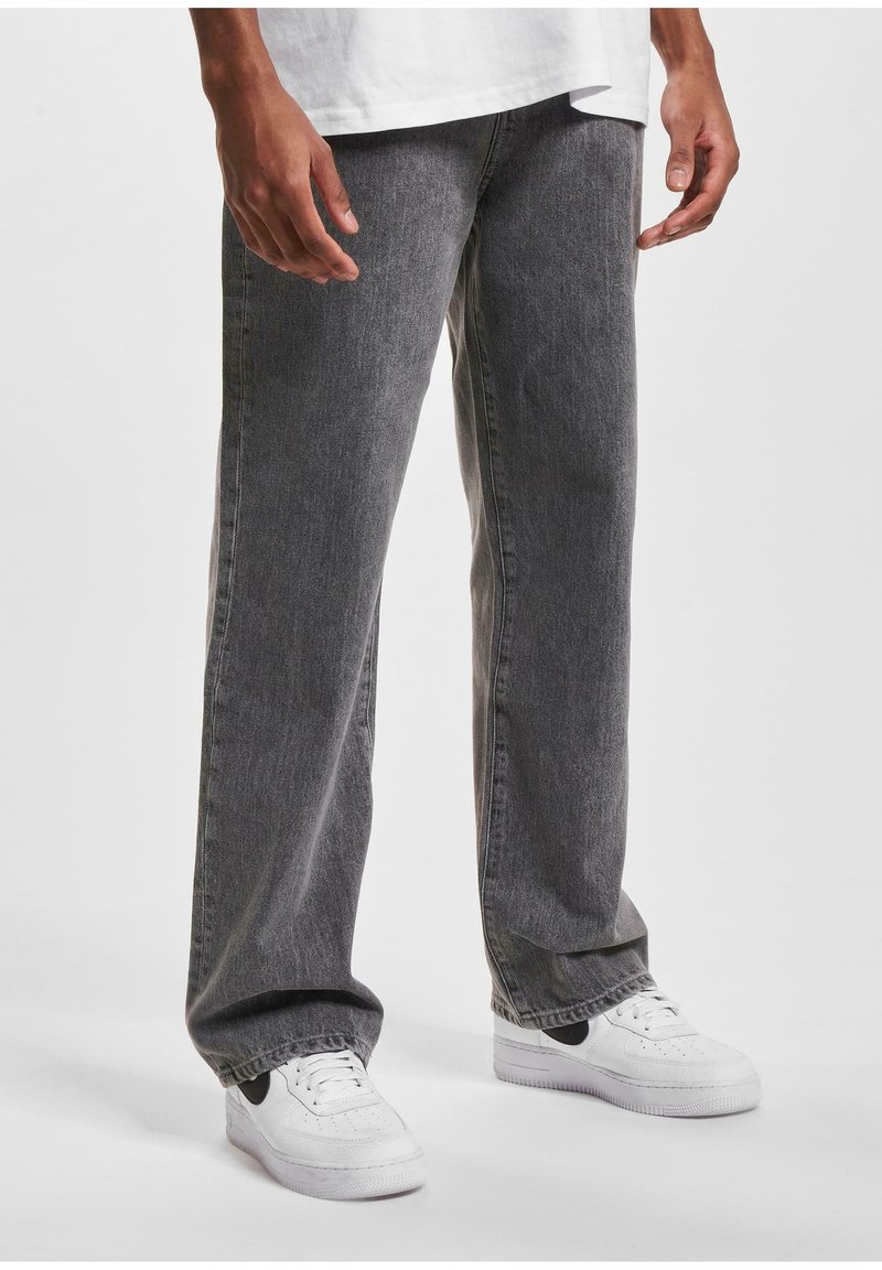 Pantalones de mezclilla gris con un corte holgado, que presentan una ligera textura y un acabado desgastado. Llevados con zapatillas blancas, que destacan un acento negro.