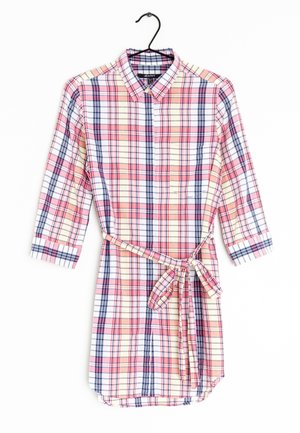 Sukienka koszulowa z długim rękawem w kratę w kolorach różowym, kremowym i granatowym, z kołnierzykiem, zapięciem na guziki z przodu oraz paskiem wiązanym w talii, wisząca na czarnym wieszaku.