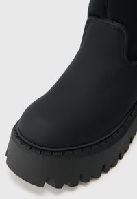 Juodos kulkšnies botai su apvaliu pirštu, matinio paviršiaus ir storesniu, briaunotu padu su tekstūruota krašto raštas.