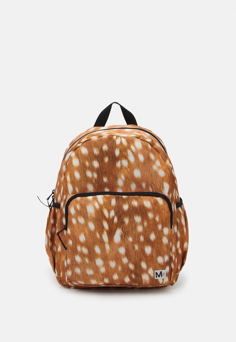 Sac à dos marron avec des taches blanches ressemblant à celles d’un cerf, poche avant zippée, tirettes de fermeture éclair noires et boucle de poignée supérieure noire sur fond uni.