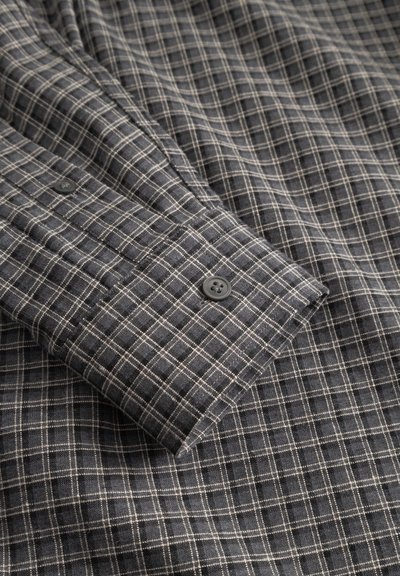 Košulja s gumbima u tamnosivoj tkanini svijetlog karo uzorka, s crnim gumbom na manžeti i glatkom teksturom.