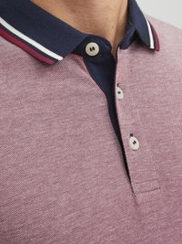 Kortærmet polo-shirt i tekstureret bordeaux stof med en marineblå krave, prydet med hvide og røde striber samt to knaplukninger.