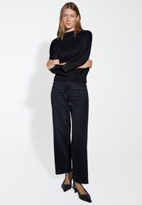 Pull noir en maille avec une finition texturée, associé à un jean large noir. Des talons noirs avec des pois blancs complètent la tenue.