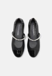 Chaussures plates noires avec un bout en cuir verni brillant, un corps en cuir texturé et une bande décorative en perles à travers le cou-de-pied.