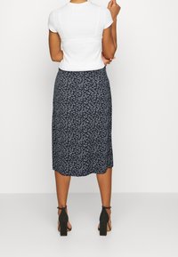 Navyfarbene Blumenshirt-Midirock mit fließendem Design und weicher Textur, kombiniert mit einem schlichten weißen Top und schwarzen Absatzsandalen.