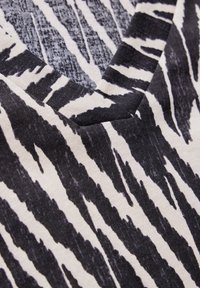 Czarno-biała dzianinowa bluzka z dekoltem w serek, w wzór w paski tygrysa, o miękkiej teksturze i mieszance jasnych i ciemnych odcieni materiału.