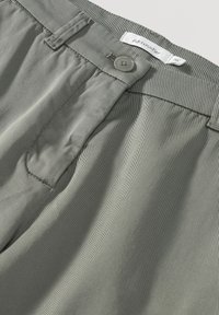 Světlá zelená tkanina s texturou, s knoflíkovým zapínáním a elastickým pasem. Disponuje vertikálními pruhy, navržena pro pohodlí a snadné nošení.