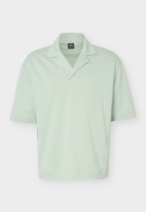 Svetlo zelena polo majica s kratkimi rokavi, zloženo ovratnico, subtilnim logotipom na prsih in zaponko z dvema gumboma.