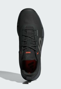 Czarne buty do biegania w terenie z teksturowaną cholewką, kontrastującymi pomarańczowymi akcentami i wyściełaną podeszwą. Posiadają wyraźne logo oraz system sznurowania.